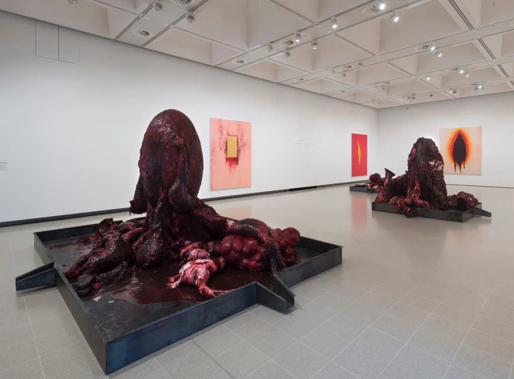two very bodily, disturbing artworks rise up in a white-walled space that also has paintings on the wall