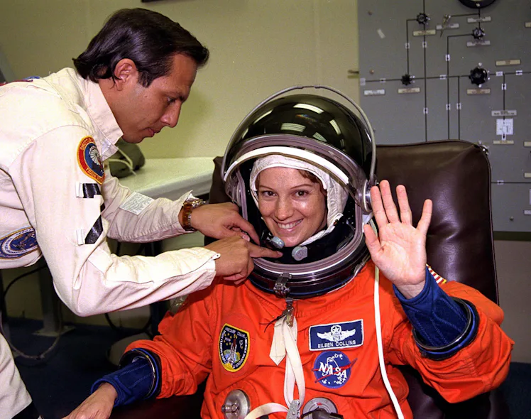 With the assistance of a suit technician, STS-84 Pilot Eileen Marie Collins finishes donning her lau...