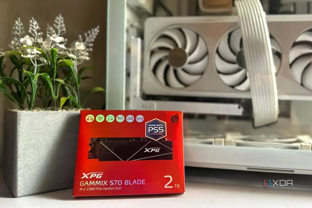 An image of a red box holding a 2TB SSD from XPG, resting against a faux flower pot and an unlit PC case.