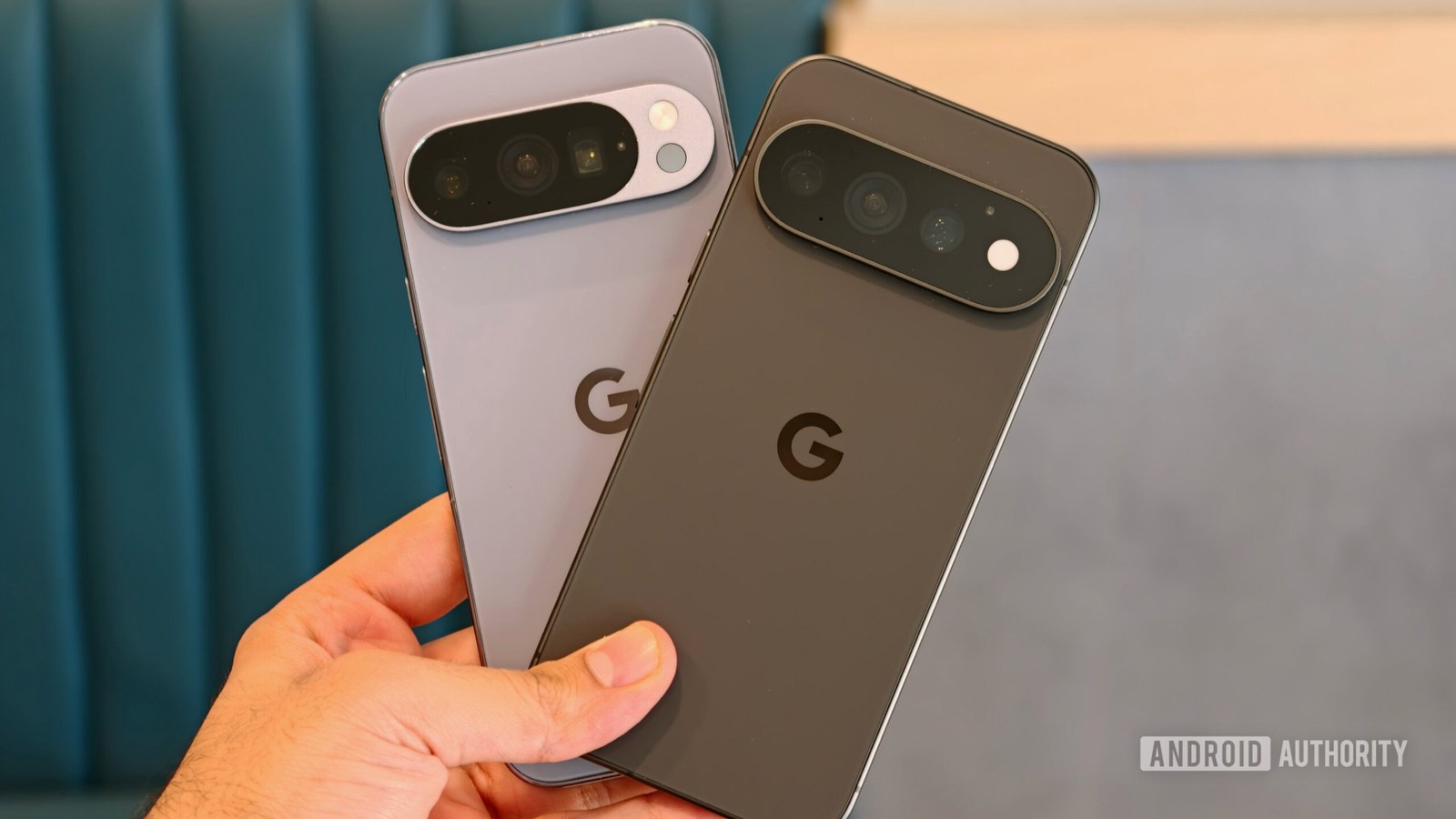 A hand holding Pixel 11 Pro and Pixel 10 Pro side-by-side to compare camera visors and rear panel designs