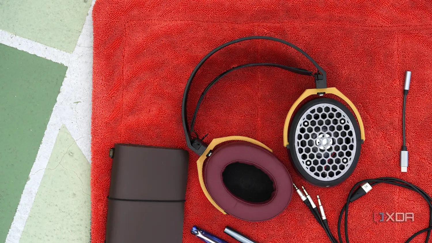 open-back 3D printed headphone grille set against a red and green backdrop with a leather notebook and cables in the frame