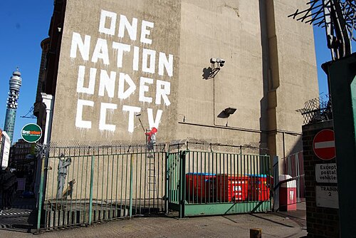 Banksy's One Nation Under CCTV graffiti, adjacent to an actual CCTV camera