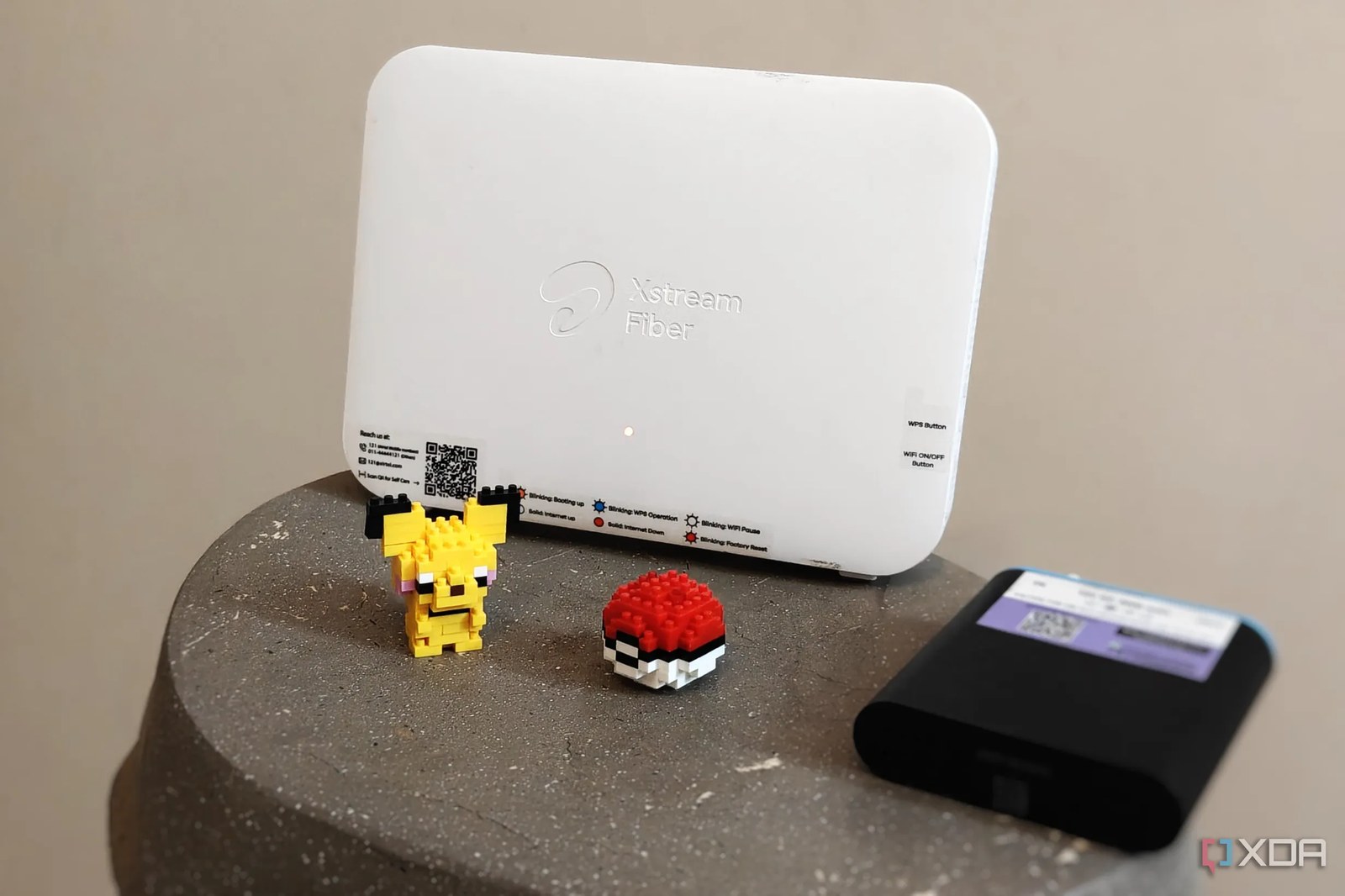 Siyah bir mini UPS ve Pikachu figürü yanına yerleştirilmiş beyaz bir Wi-Fi yönlendiricisinin yakın planı