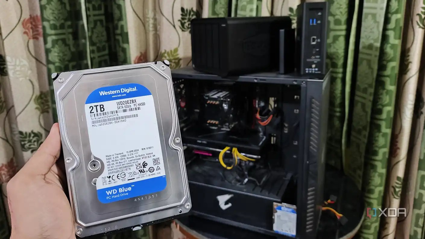 A person holding an HDD in front of a PC and two TerraMaster NAS units